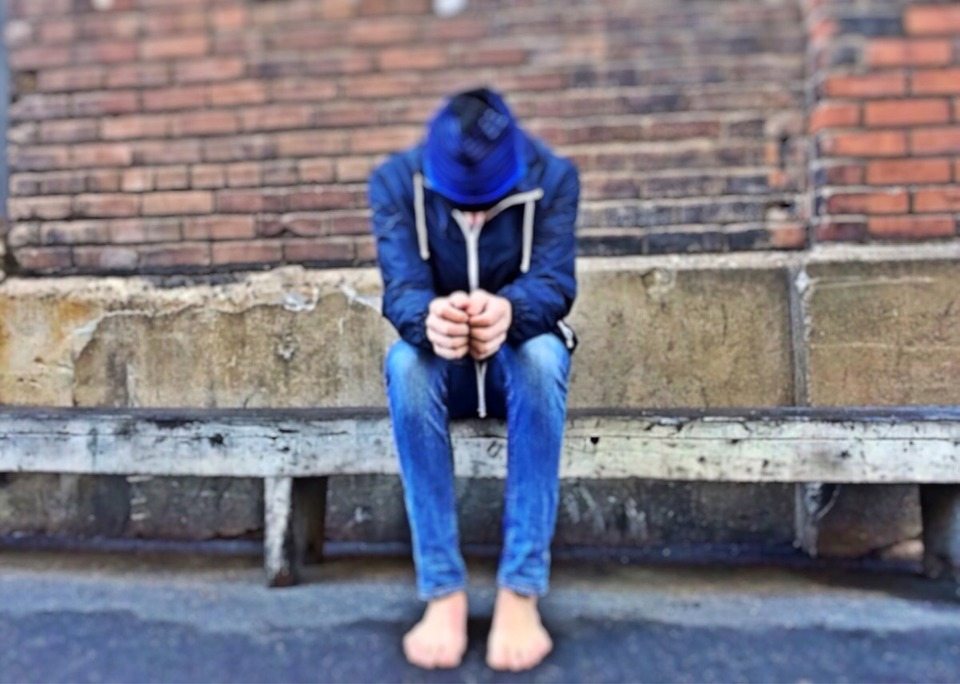 Bullied teen sitting on cement slab on city street