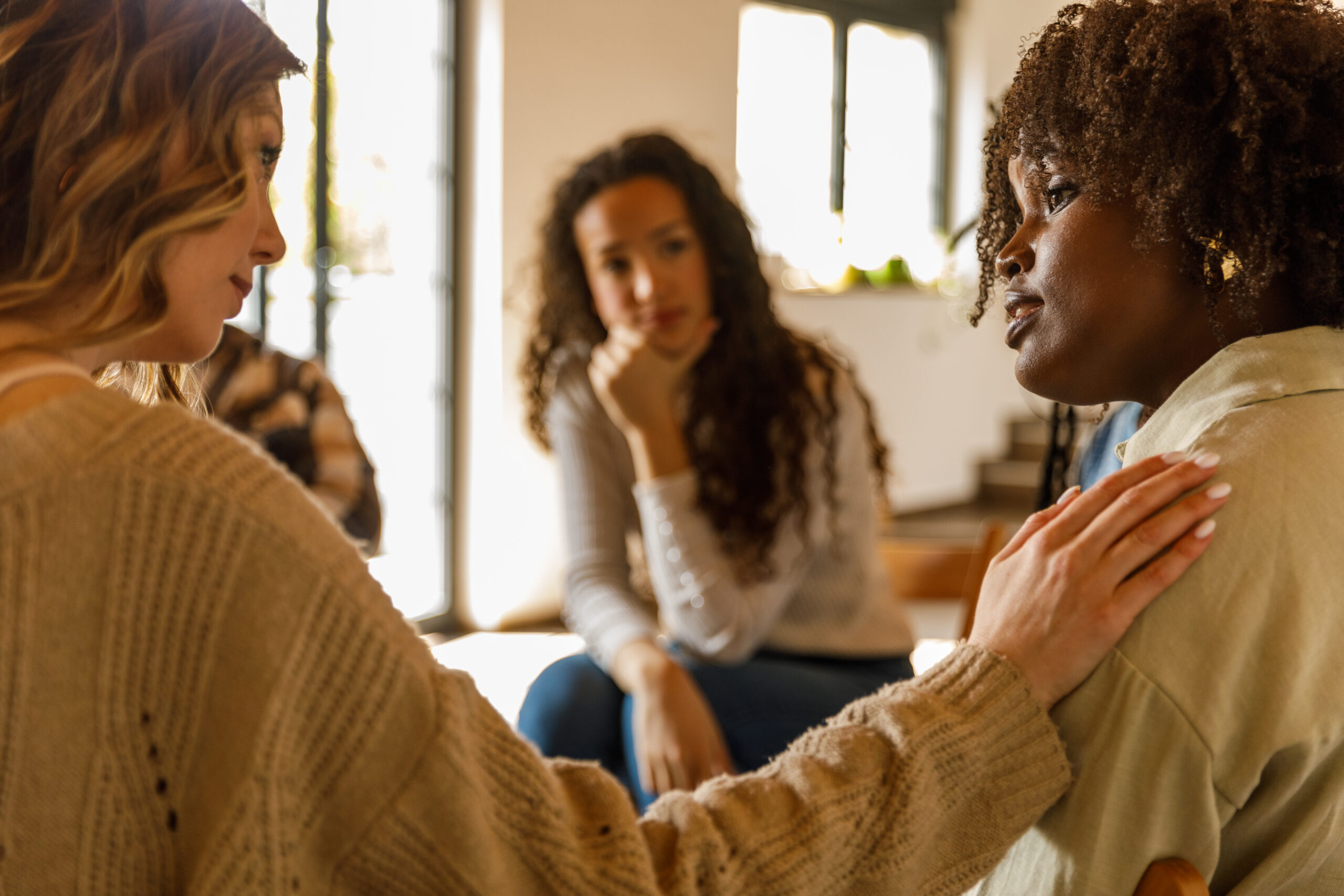 Compassionate woman holding hand on friend’s shoulder during a group therapy session